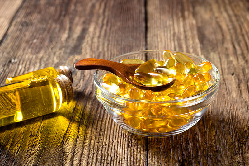 Glass bowl with yellow gel capsules and a wooden spoon on a wooden surface