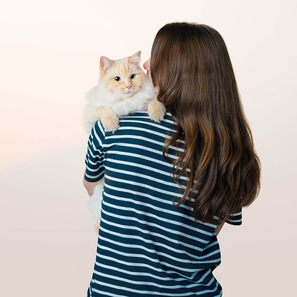 Woman holding a fluffy cat on her shoulder against a plain background